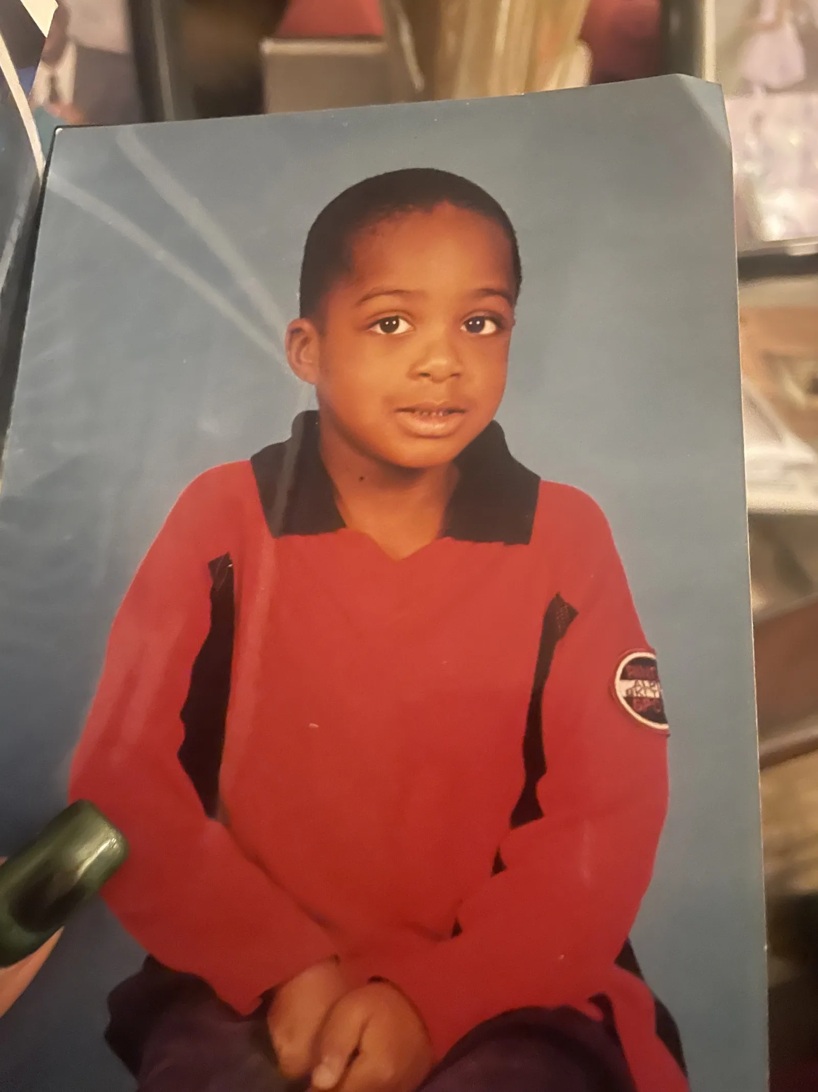 The unedited source photograph: a printed studio portrait of a young child in a red shirt with a black collar, seated against a blue background.
