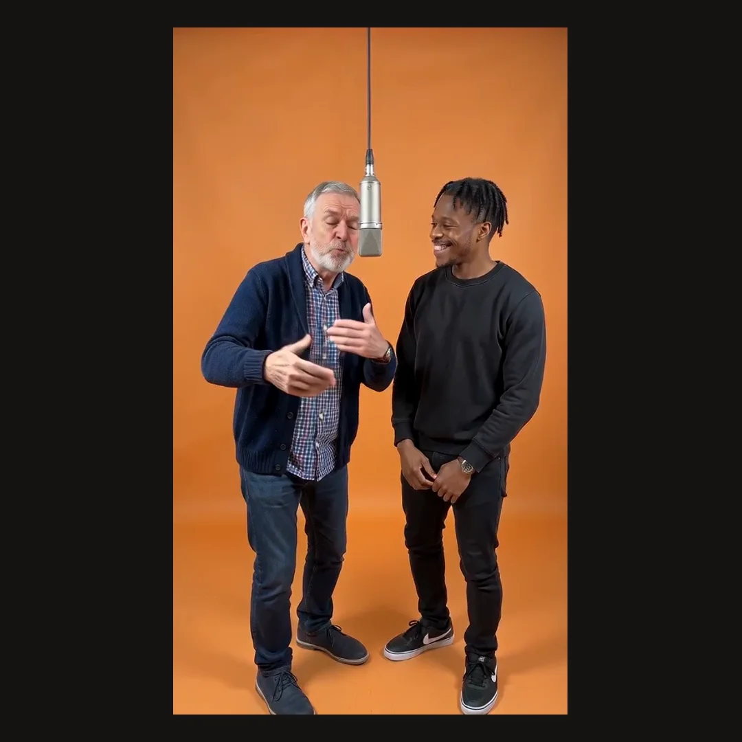 The same two men generated into an orange studio booth, sharing a microphone that hangs from the ceiling
